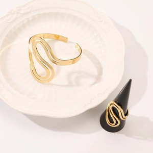 Detailed close-up of golden wavy cuff bracelet and ring set on an elegant display stand