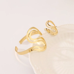 Detail of gold double-layered S-shaped open bracelet and ring set on ceramic plate
