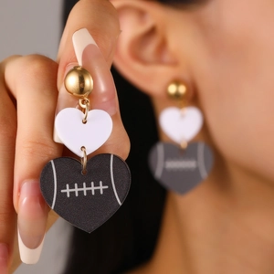 Close-up of heart-shaped acrylic earrings with American football pattern and gold studs