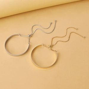 Detail of adjustable minimalist leaf metal bangles with gold and silver finish on beige background