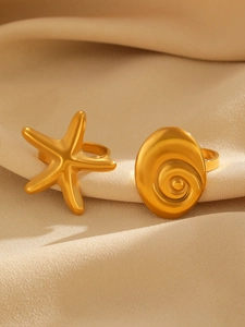 Close-up of golden starfish and spiral seashell adjustable rings on silk fabric