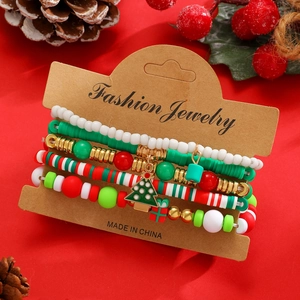 Dettaglio di braccialetti natalizi a strati con ciondoli albero e regalo su sfondo rosso