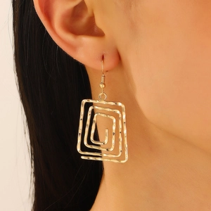 Close-up of golden geometric hollow rectangle spiral earrings with hammered metal texture