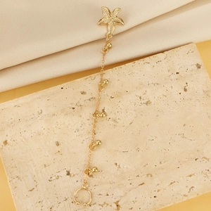 Elegante orecchino a stella marina dorata con catena a sfere e clip su sfondo di seta beige
