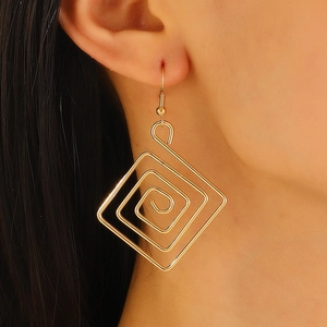 Close-up of golden spiral square geometric drop earrings worn by a female model