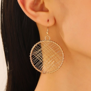 Detail of large gold mesh earrings with woven hollow design worn by a model