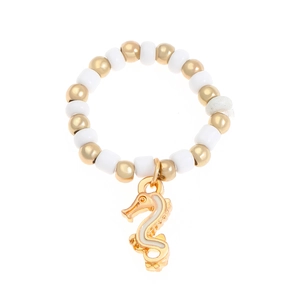 Detail of beaded ring with gold sea horse charm and white cylinder beads in macro view