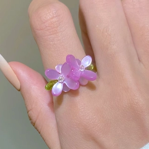 Macro detail of handmade beaded ring with purple resin flowers and green beads