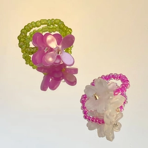 Detail view of two colorful beaded rings with flower charms on a reflective mirror base