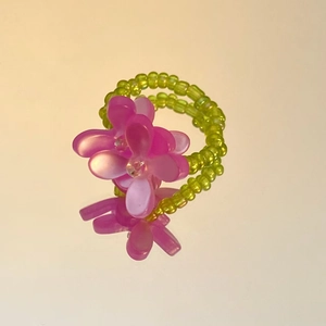 Detailed close-up of handmade beaded ring with soft green beads and purple resin flowers