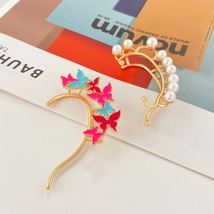 Detalle de pendientes de hoja dorada con mariposas de colores y perlas elegantes
