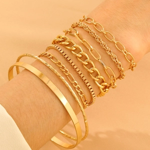 Close-up of stacked gold knot bracelets and layered geometric chains on female wrist