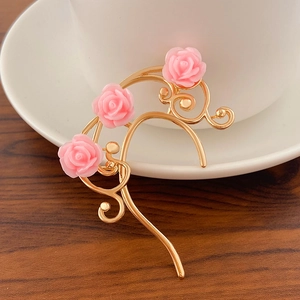 Detalle de pendiente de hoja dorada con rosas de resina rosa sobre superficie de madera
