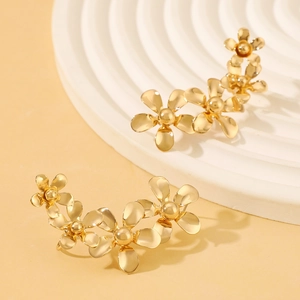 Pendientes de flores doradas vintage con tres pétalos sobre pedestal blanco