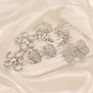 Set of four textured silver alloy floral earrings displayed on elegant white silk fabric