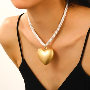 Close-up of a large polished gold 3D heart pendant necklace with white twisted rope