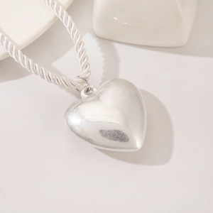 Macro view of a 3D silver heart pendant on a white braided rope necklace cord
