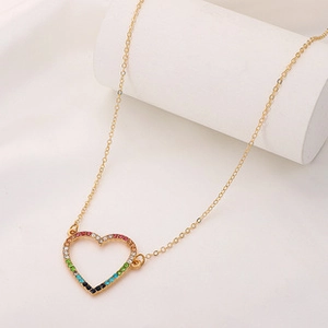 Nahaufnahme der goldenen Kette mit regenbogenfarbenem Herzanhänger auf weißem Stoff