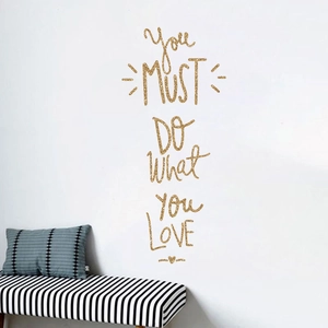 Detail of gold glitter 'Do What You Love' wall sticker on a clean white wall