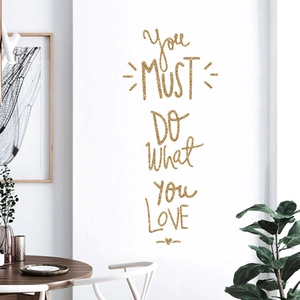 Macro detail of gold glitter 'You MUST DO What YOU LOVE' wall decal in a home office