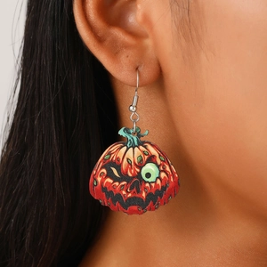 Close-up of wooden Halloween pumpkin earrings with a green eyeball on a model's ear