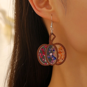 Detail of wooden pumpkin earrings with colorful glitter sequins worn by a model