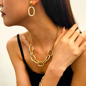 Primer plano de un elegante collar de cadena dorada gruesa y pendientes ovalados en modelo