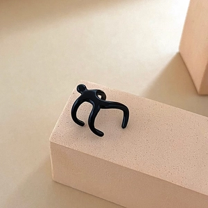Minimalist black glazed human-shaped ear cuff on a matte pink geometric display stand