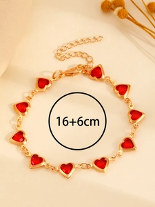 Detalle de una pulsera de corazón dorada con piedras rojas y cadena ajustable 16+6cm