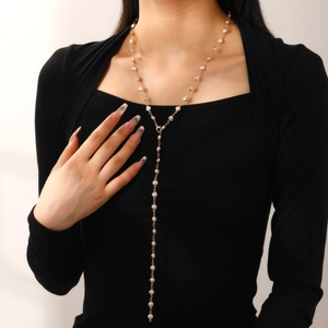 Elegante collar largo en Y dorado con perlas blancas sobre una modelo en ropa negra