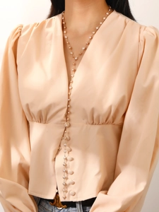 Primer plano detallado de un collar largo en forma de Y dorado con perlas blancas en una modelo