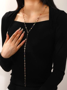 Collar largo en Y dorado con gemas de colores sobre un jersey negro de cerca