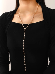 Detalle de collar largo dorado en forma de Y con perlas sobre una prenda negra