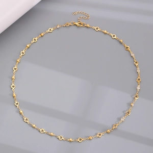 Detalle de un collar dorado con eslabones de corazón, circonitas y cierre de mosquetón
