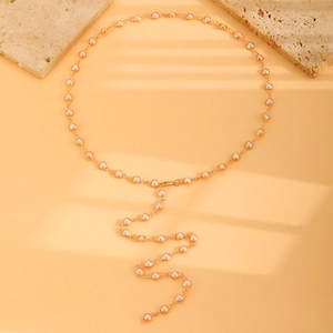 Nahaufnahme der goldenen Y-Kette mit Perlen vor elegantem Licht- und Schattenspiel