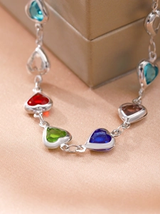 Detalle de pulsera plateada con gemas de colores en forma de corazón sobre seda