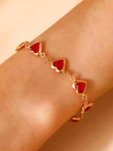 Détail d'un bracelet doré avec des pierres rouges en forme de cœur au poignet d'une femme