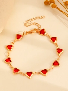 Détail macro d'un bracelet doré avec cœurs en pierres rouges et fermoir mousqueton