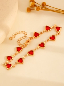 Detalle de pulsera de corazón dorada con cristales rojos y cierre de mosquetón ajustable