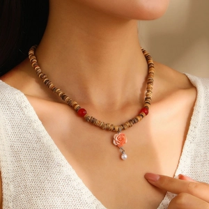 Close-up of wooden bead prayer necklace featuring a pink rose pendant and red accent beads