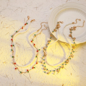 Détail de colliers de perles superposés avec pendentifs cœur et perles colorées sur fond beige