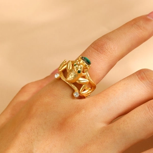 Detailed view of a gold frog ring holding a green emerald heart gemstone on a finger