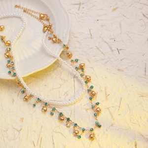 Détail du collier doré multi-rangs avec perles, strass bleus et pendentif en forme de cœur