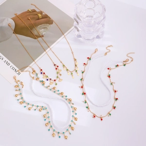 Détail de colliers dorés multicouches avec perles, strass colorés et pendentif coquillage