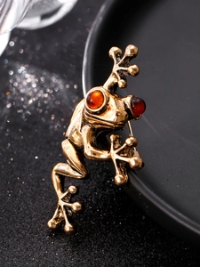 Macro side view of vintage gold frog brooch with red eyes and detailed textured finish
