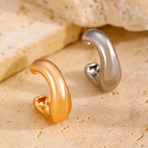 Detalle de pendientes de clip gruesos en forma de C en oro y plata sobre piedra