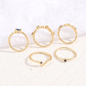 Detailansicht eines fünfteiligen Goldring-Sets mit blauen Edelsteinen auf Sandstruktur