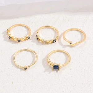 Detailansicht eines fünfteiligen vergoldeten Ring-Sets mit blauen Strasssteinen auf Textur