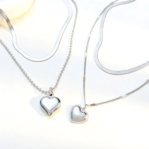 Close-up of silver layered heart pendant necklaces with snake chain and love engravings