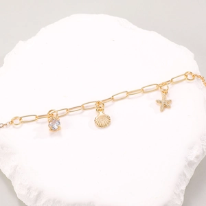 Dettaglio della collana dorata con pendenti a stella marina e conchiglia in zircone su roccia